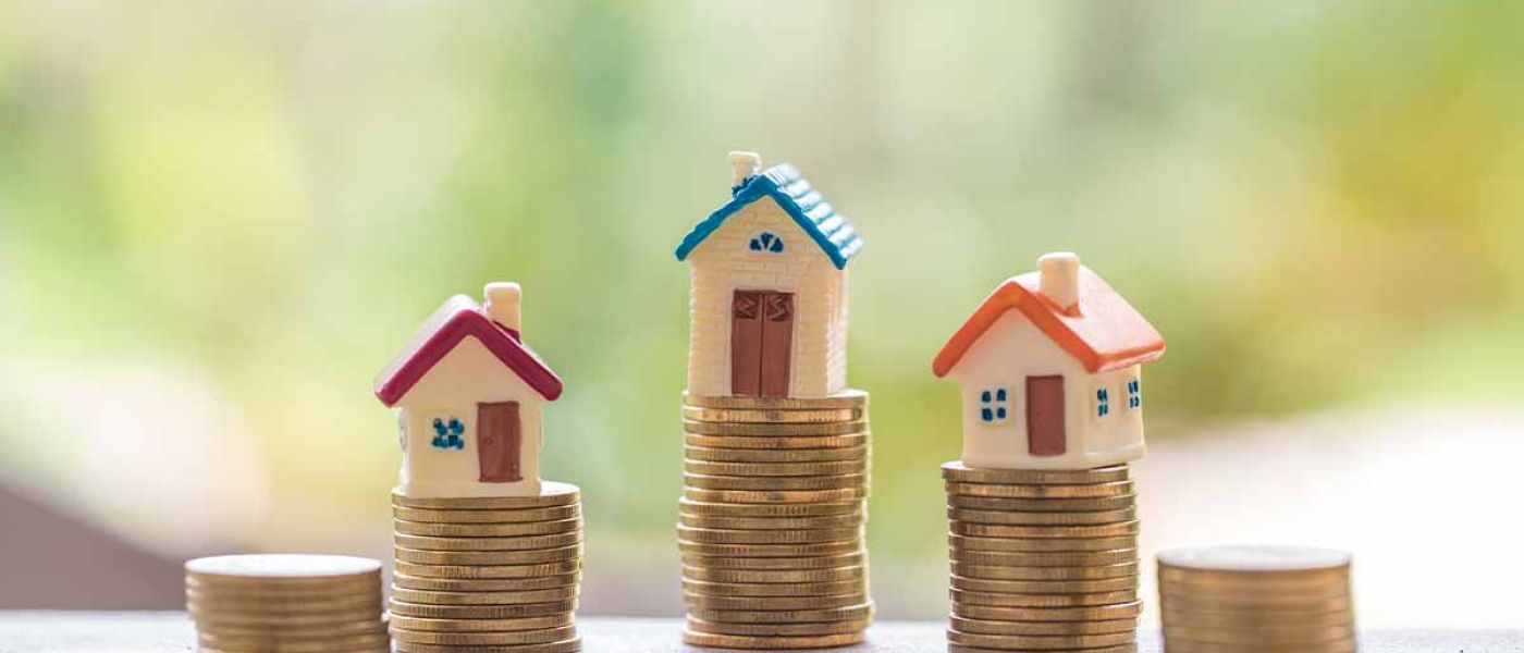 Drei Modellhäuschen stehen auf Stapeln von Münzen - Immobilienfinanzierung