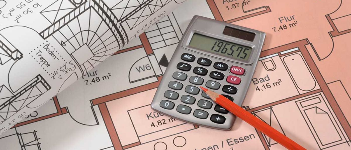 Auf dem Grundrissplan einer Immobilie liegen ein weiterer zusammengerollter Grundrissplan, ein Taschenrechner und ein Stift | Immobilienfinanzierung