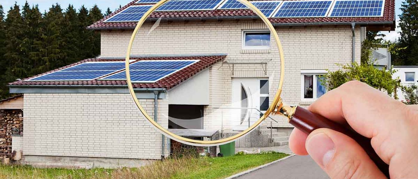 Eine Hand mit Lupe vor einem Haus mit Garage - Suchauftrag